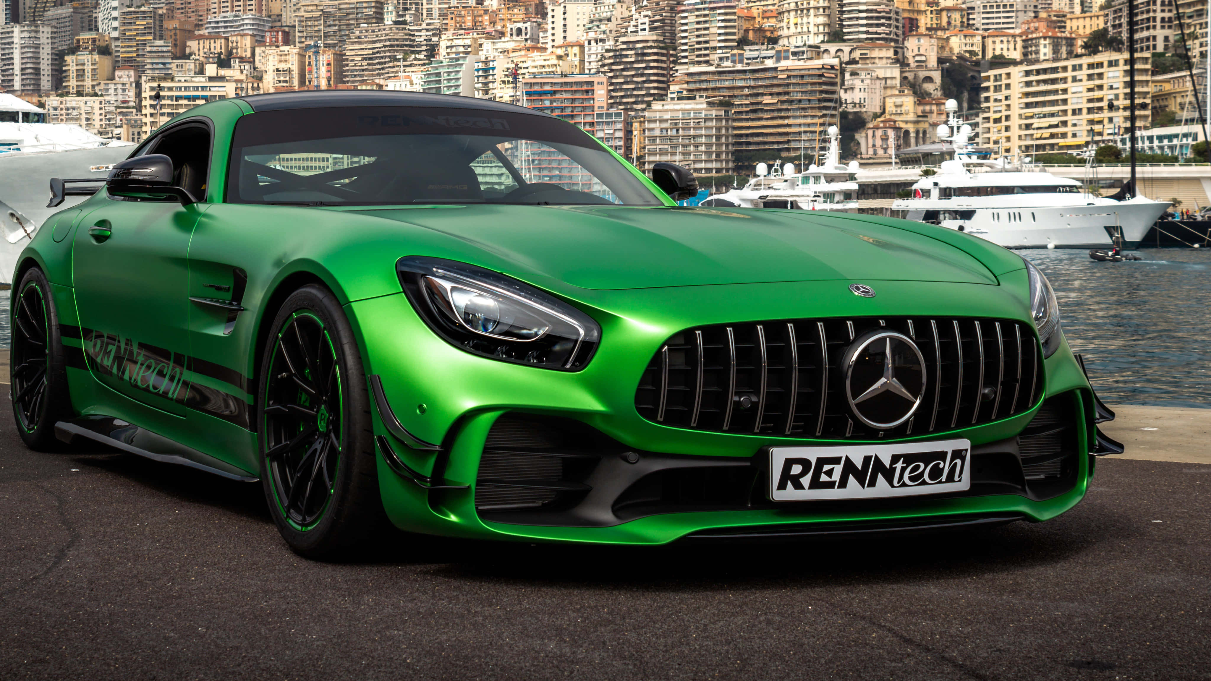 流線型綠色梅賽德斯-AMG GT R 賽車背景 壁紙 — 一架鮮綠色、經RENNtech改裝的Mercedes-AMG GT停泊在港口旁，背景是豪華遊艇和密集的城市景觀。
