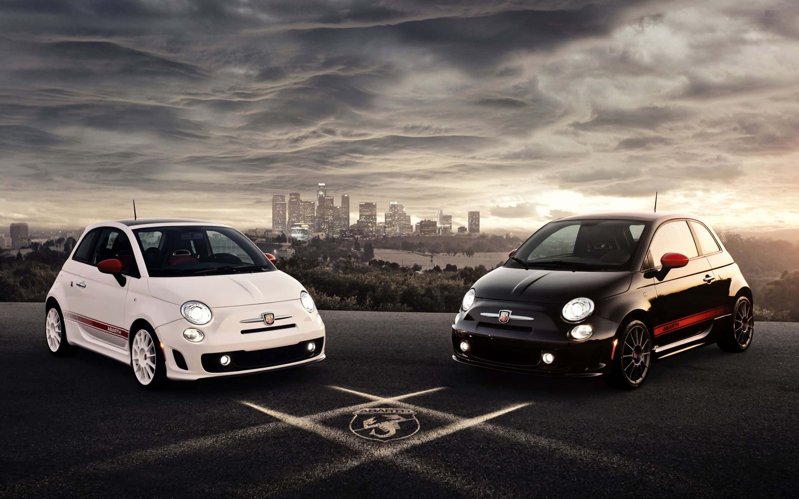 流線型菲亞特500L行駛中 壁紙 — 兩輛白色和黑色帶紅色點綴的Fiat 500汽車停在瀝青路上，背景是夕陽下戲劇性的多雲天空和城市天際線。