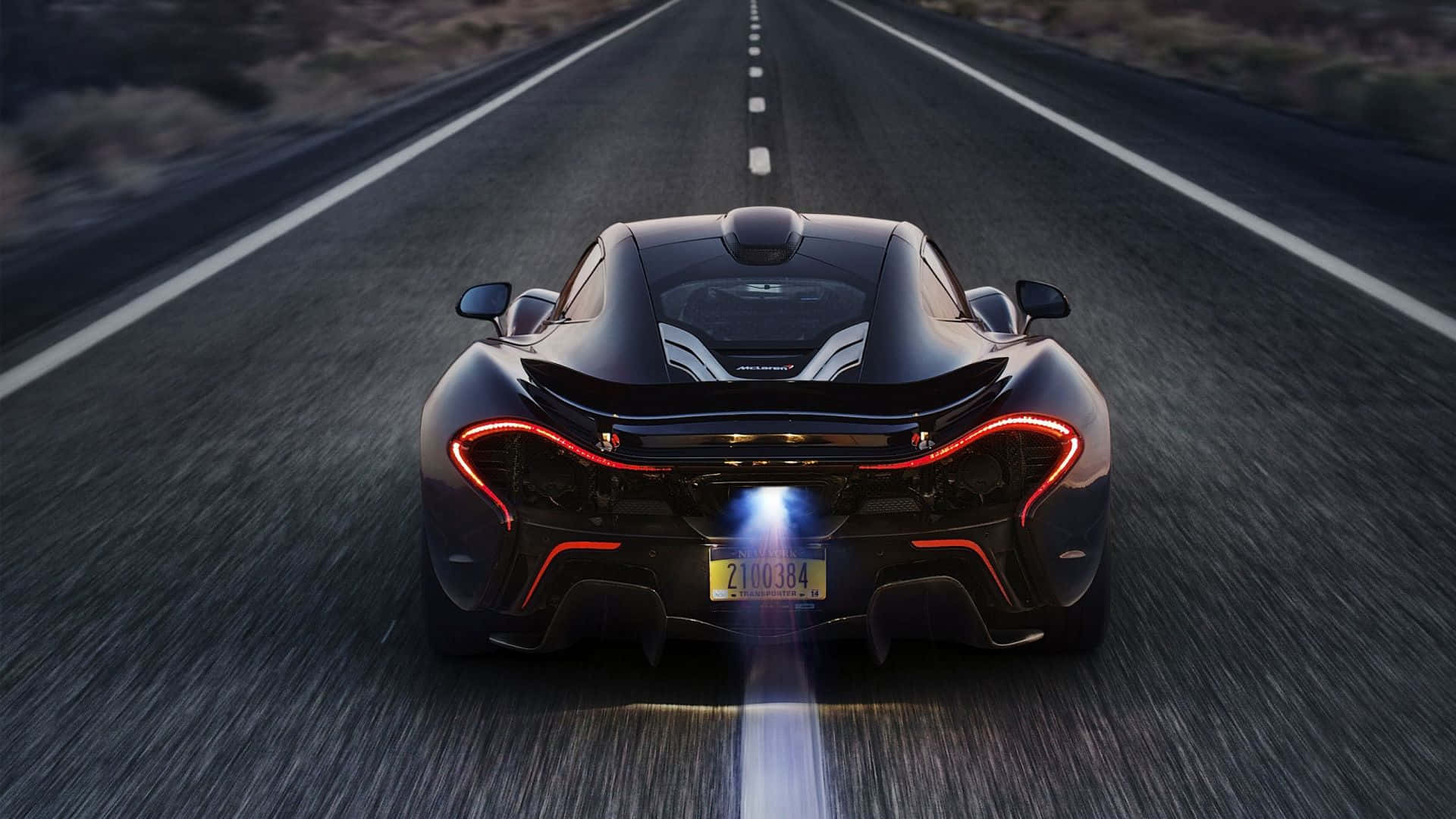 黑色McLaren P1在黃昏時分於沙漠公路飛馳，帶有發光尾燈。