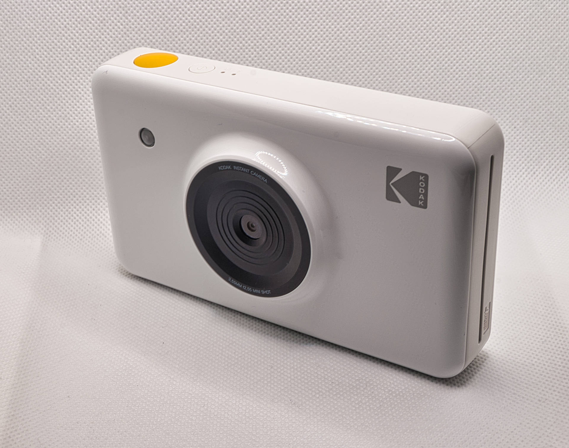 白色Kodak即影即有相機，帶有黃色快門按鈕，置於紋理背景上
