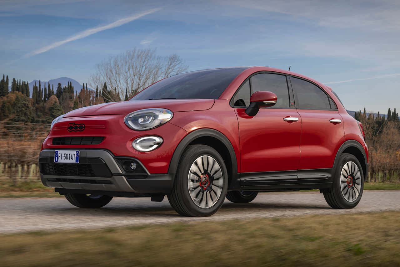 流線時尚的菲亞特 壁紙 — 一輛鮮紅色的Fiat 500X SUV在鄉村道路上行駛，背景有模糊的綠化和遠處的山脈，天空清澈湛藍。