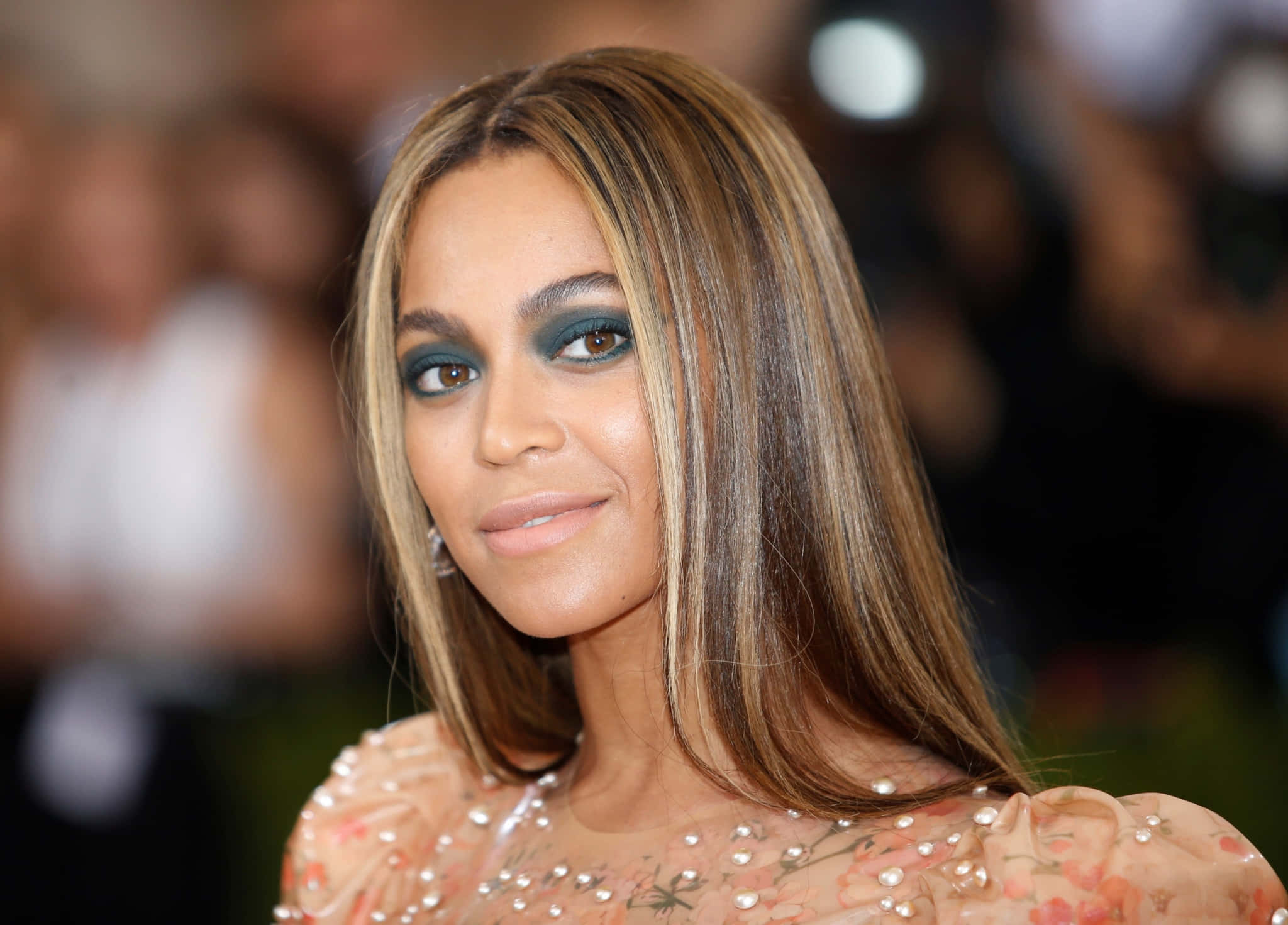 流行天后——傳奇碧昂絲 壁紙 — Beyoncé 在一個華麗的活動中，穿著花卉珠飾長袍，搭配大膽的青綠色眼妝，溫柔地微笑。