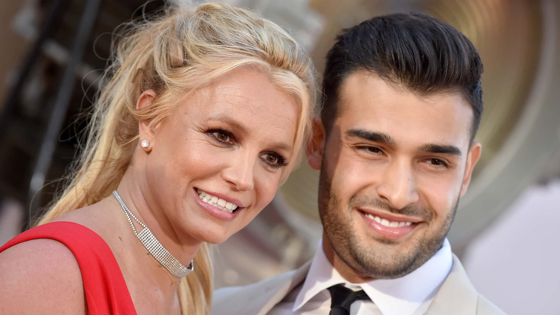 Britney Spears 和 Sam Asghari 在紅地毯活動中穿著正裝微笑。