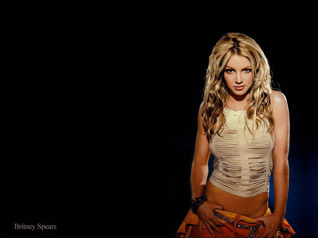Britney Spears 身穿破爛的米色上衣和橙色裙子，背景為黑色。