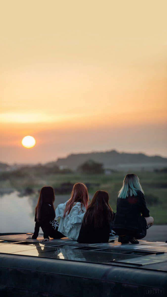 流行文化偶像：BLACKPINK 壁紙 — 四個朋友坐在車頂上，看著夕陽落在平靜的湖面和遠處的山丘上。