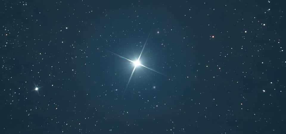 浩瀚宇宙中的閃耀星群 壁紙 — 一顆帶有輻射尖刺的明亮恆星主導著深藍色星場，點綴著遠處閃爍的燈光。