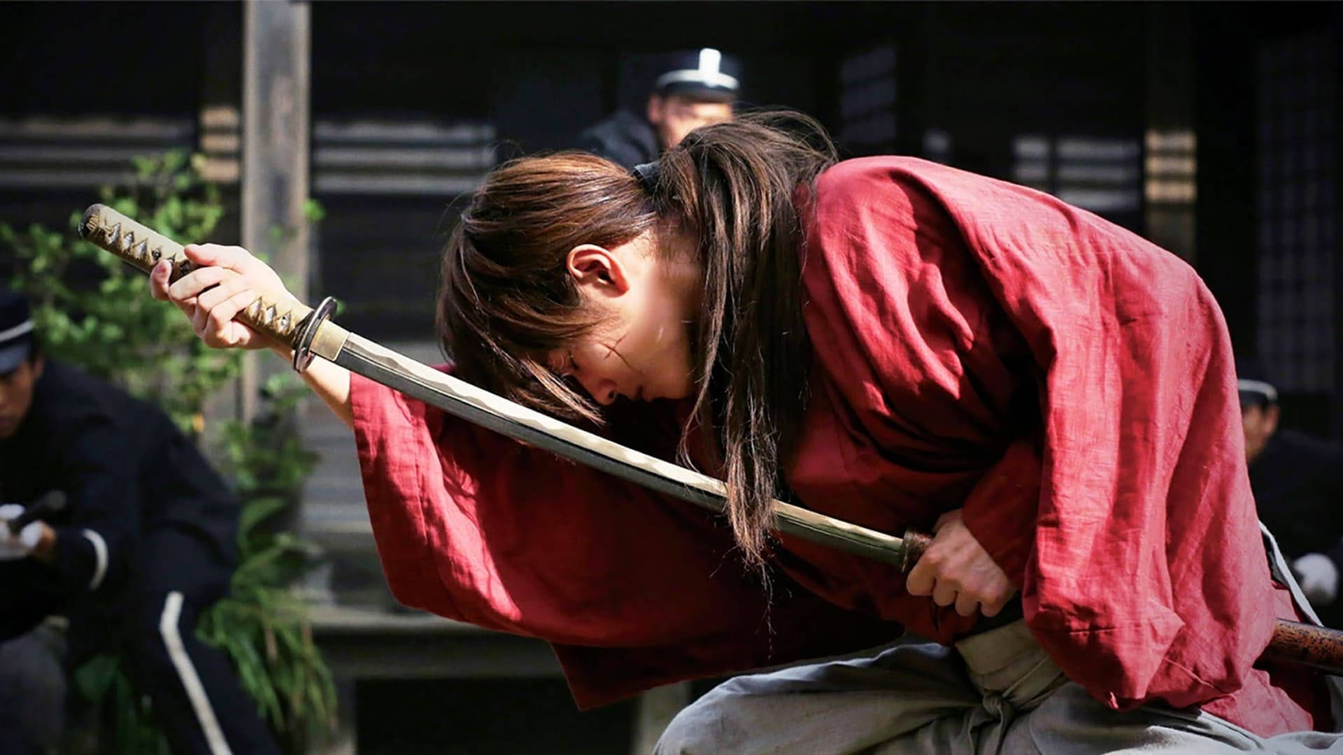 《浪客劍心》收劍瞬間 壁紙 — 一位身穿紅袍的武士在傳統日本庭院中深深鞠躬，同時緊握著一把武士刀。