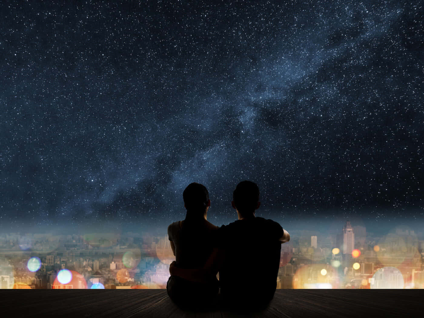 情侶剪影映襯著發光城市上方的星空夜空。