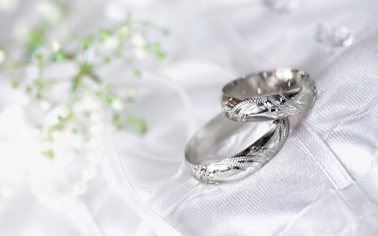 浪漫銀婚戒 壁紙 — 兩隻精雕細刻的銀色結婚戒指放在柔軟的白色布料上，旁邊是精緻的滿天星花朵。