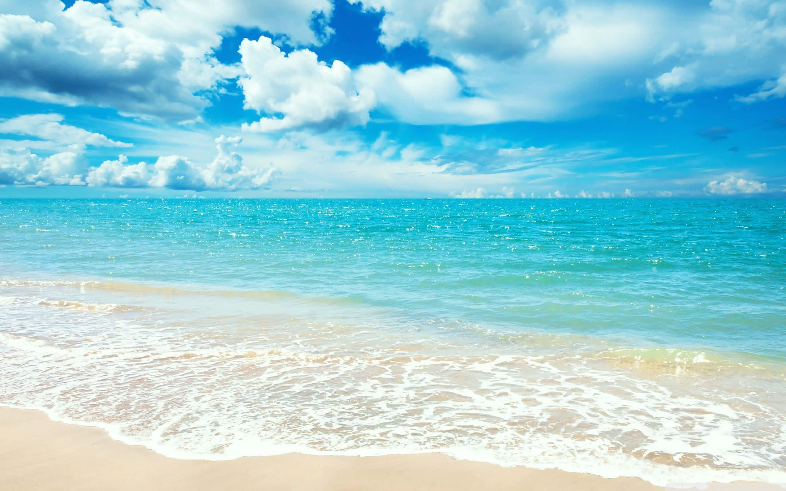 浪花與雲朵的海灘 壁紙 — 陽光普照的碧綠海浪輕輕拍打著金色沙灘，天空湛藍，點綴著蓬鬆的白雲。