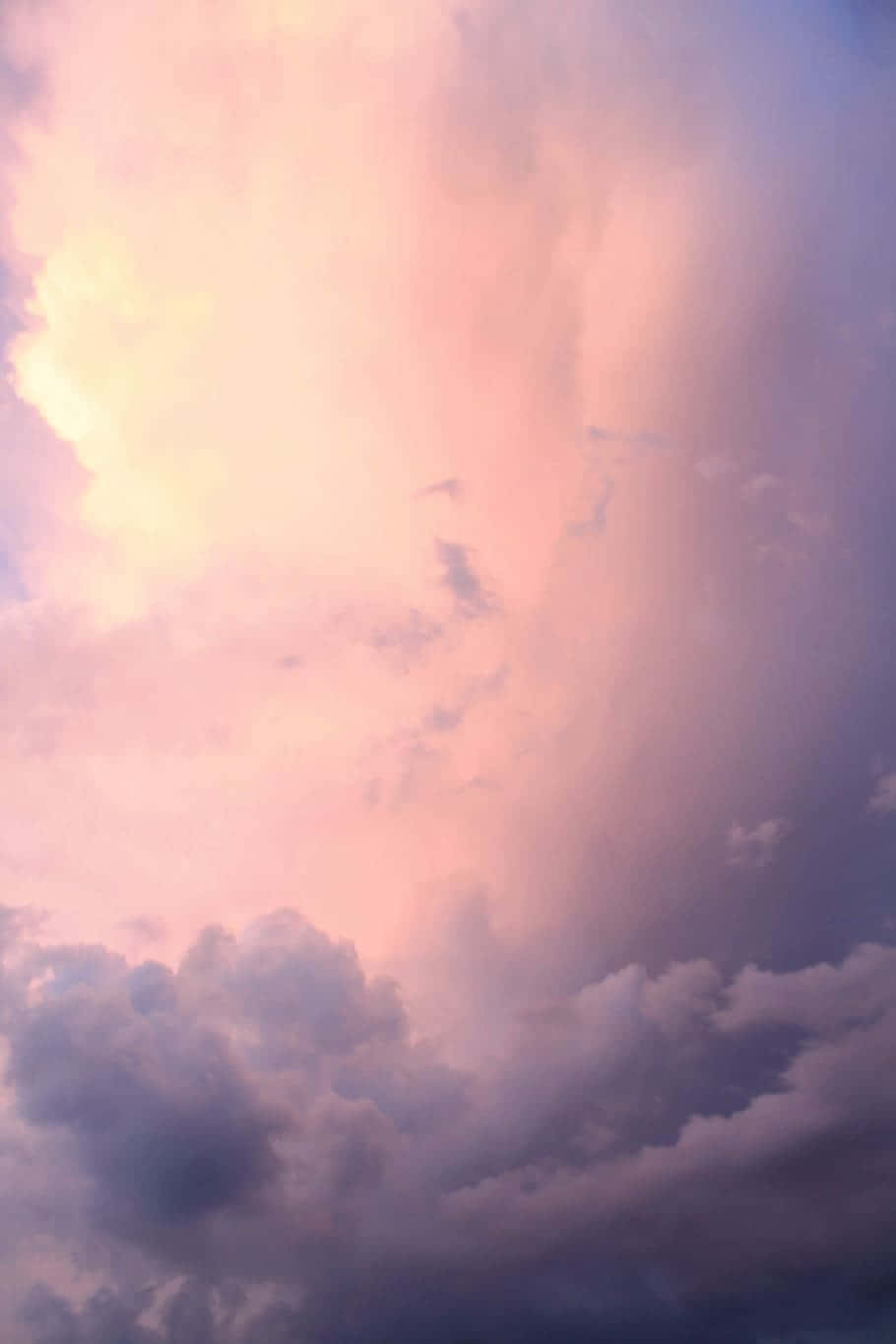 浮於雲端，尋找你的個人風格 壁紙 — 一幅戲劇性的天空，塗上柔和的粉紅、紫色和黃色調，陽光穿過蓬鬆的雲層。