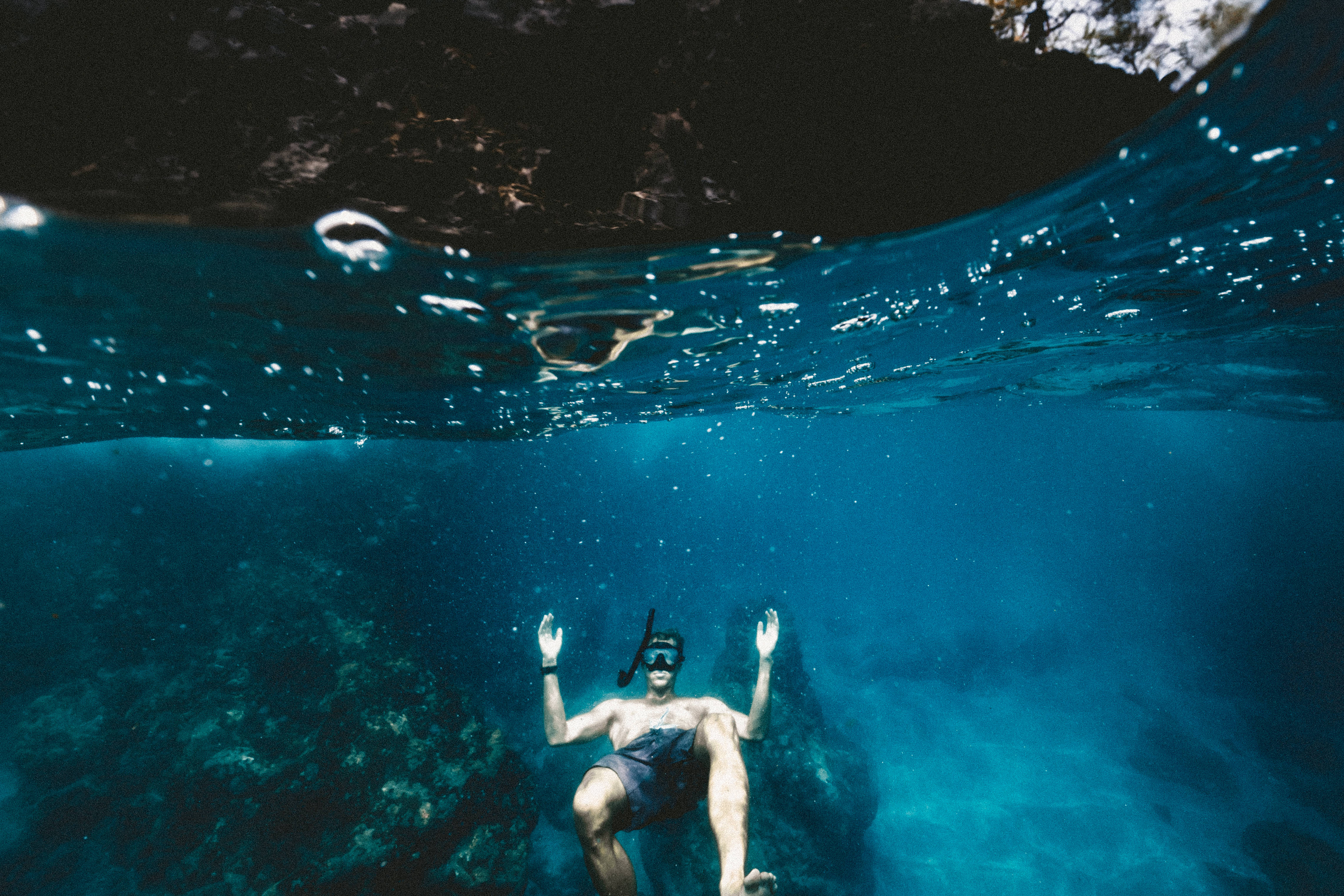 浮潛仰躺漂浮 壁紙 — 一名浮潛者在陽光照射的水面下平靜地漂浮，雙臂舉起，在清澈的碧綠海水中充滿驚奇。