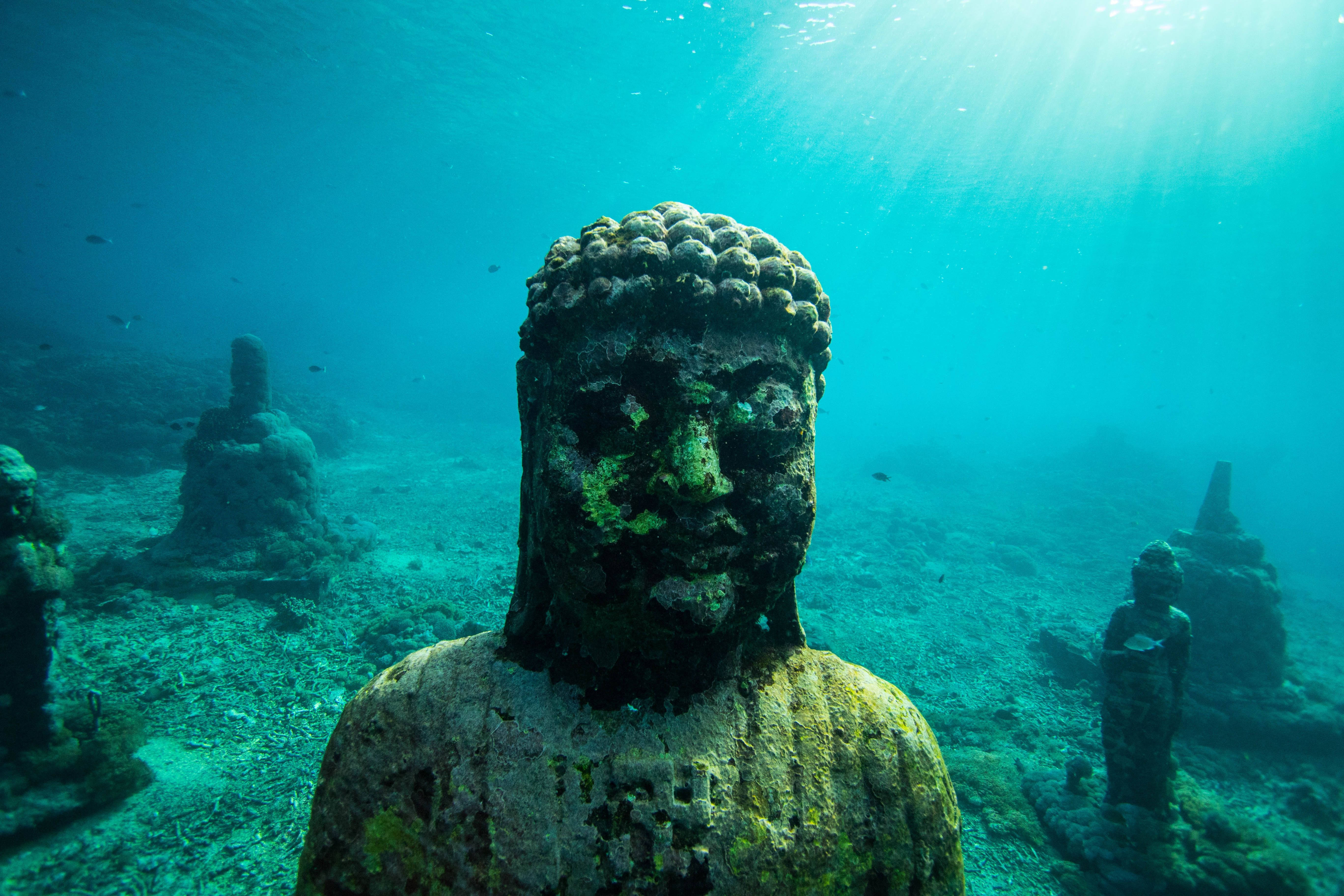 浮潛佛像 壁紙 — 被藻類覆蓋的古老佛像躺在陽光照射的海底，光線穿透碧綠的海水。