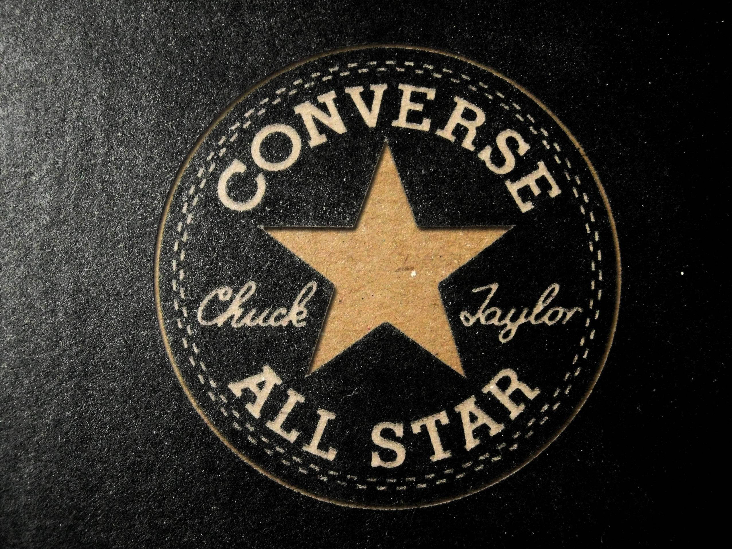 浮雕匡威標誌 壁紙 — 經典 Converse All Star 標誌布章的近距離特寫，在帶有紋理的黑色布料上，有米色星星和縫線。