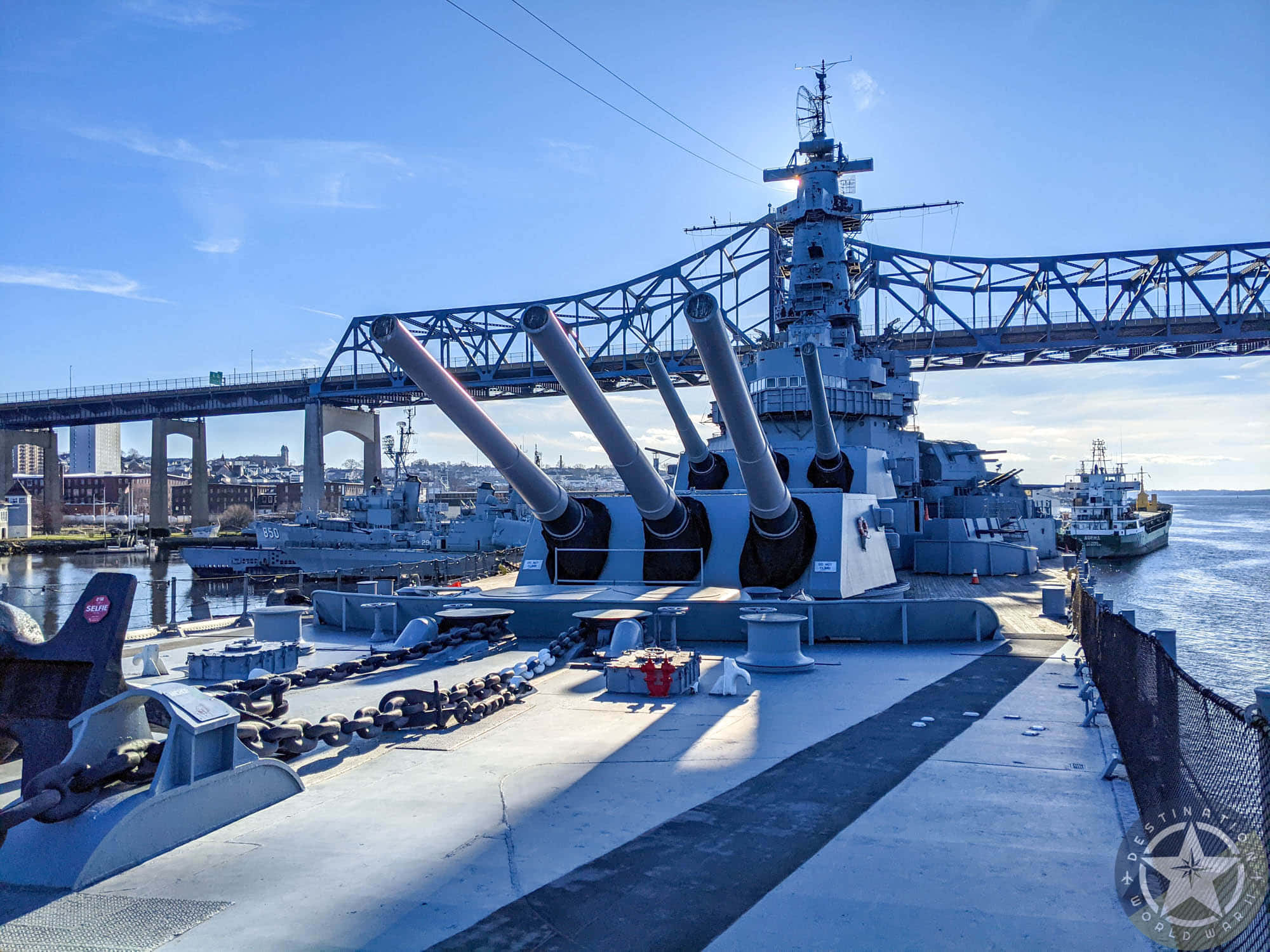 海上巨艦——戰艦駛向遠方 壁紙 — 一艘巨大的戰艦，擁有高聳的炮塔，停泊在藍天下，上方有拱形橋樑。