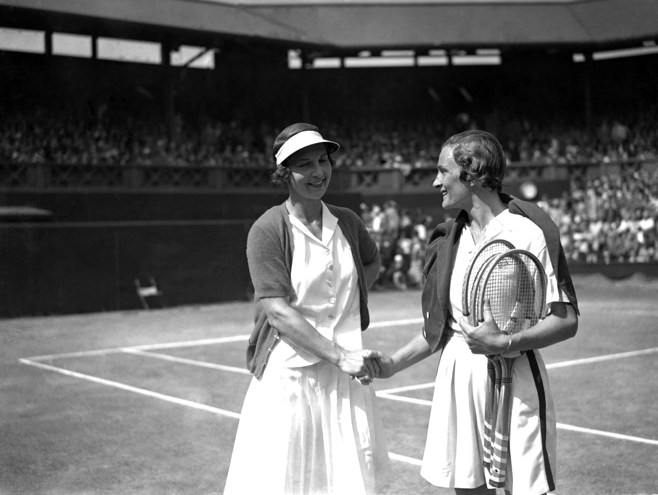 海倫·威爾斯與海倫·雅各布斯1935年溫布頓賽事 壁紙 — 兩位復古網球選手在陽光明媚的草地場上握手，身後是座無虛席的體育場。