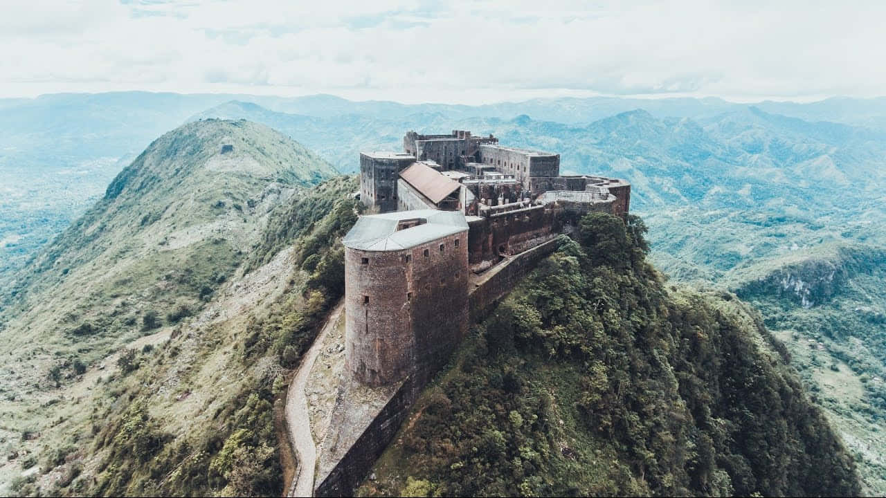 海地山脈上的歷史性拉弗里耶爾城堡 壁紙 — 一座歷史悠久的石頭堡壘戲劇性地坐落在鬱鬱蔥蔥的山脊頂端，俯瞰著廣闊的山谷。