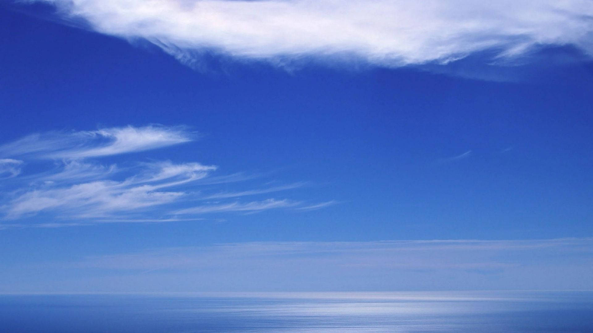 海天交界天際線 壁紙 — 廣闊平靜的海洋在柔和縷縷雲朵下與無盡天空相遇，呈現寧靜的日光。
