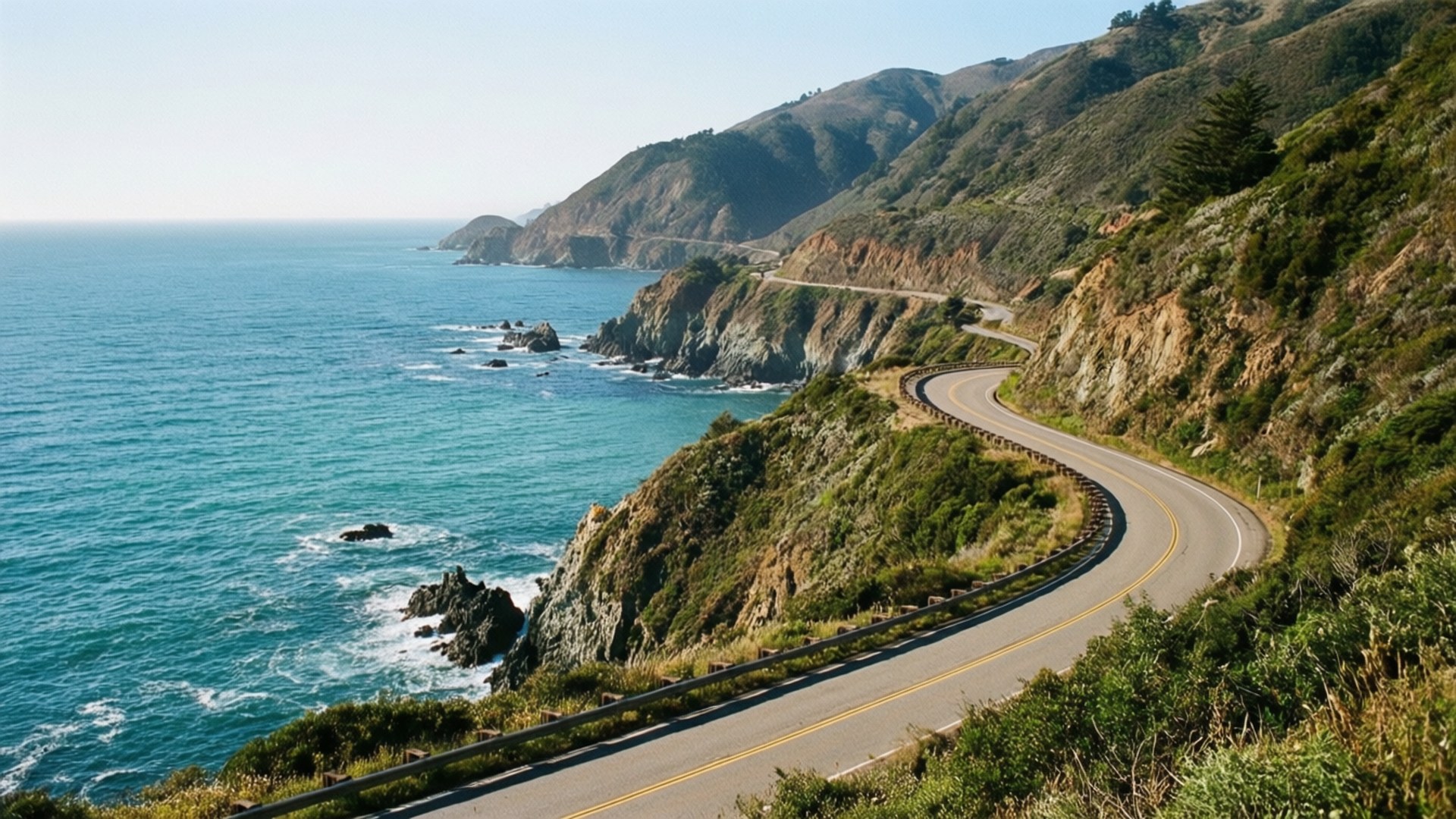 海岸公路駕駛 壁紙 — 一條蜿蜒的海岸公路緊貼陡峭的懸崖，俯瞰著在清澈藍天下拍打岩石海岸的碧綠海浪。