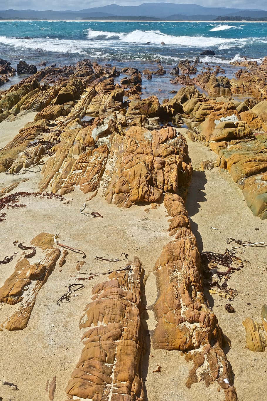 海岸岩層地質景觀 壁紙 — 陽光明媚的海灘，崎嶇的橙色岩石和碧綠色的海浪拍打著沙灘。