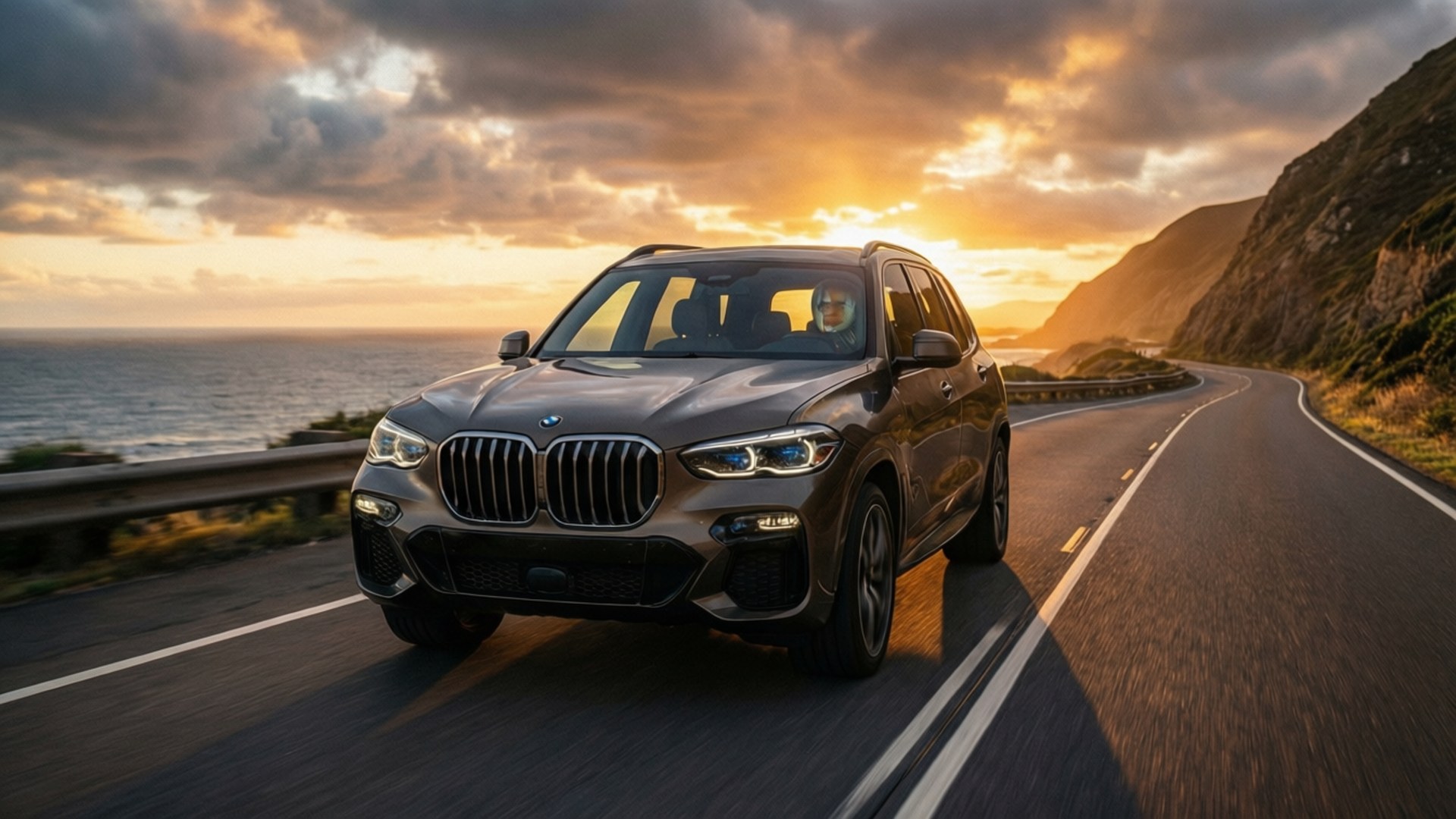 灰色BMW SUV在金色日落中行駛於海岸公路。