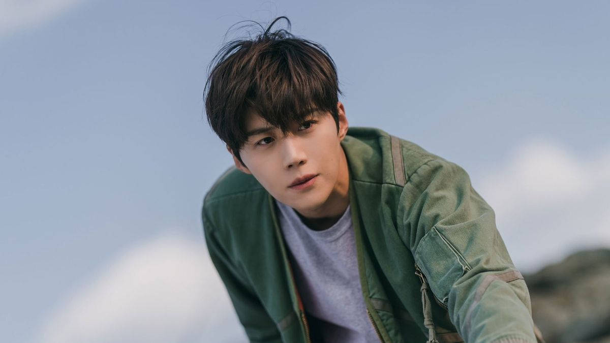 《海岸村恰恰恰》男主角 壁紙 — 一個年輕男子，一頭凌亂的黑髮，身穿綠色外套，在柔和的藍天和 fluffy 白雲背景下向前傾身。