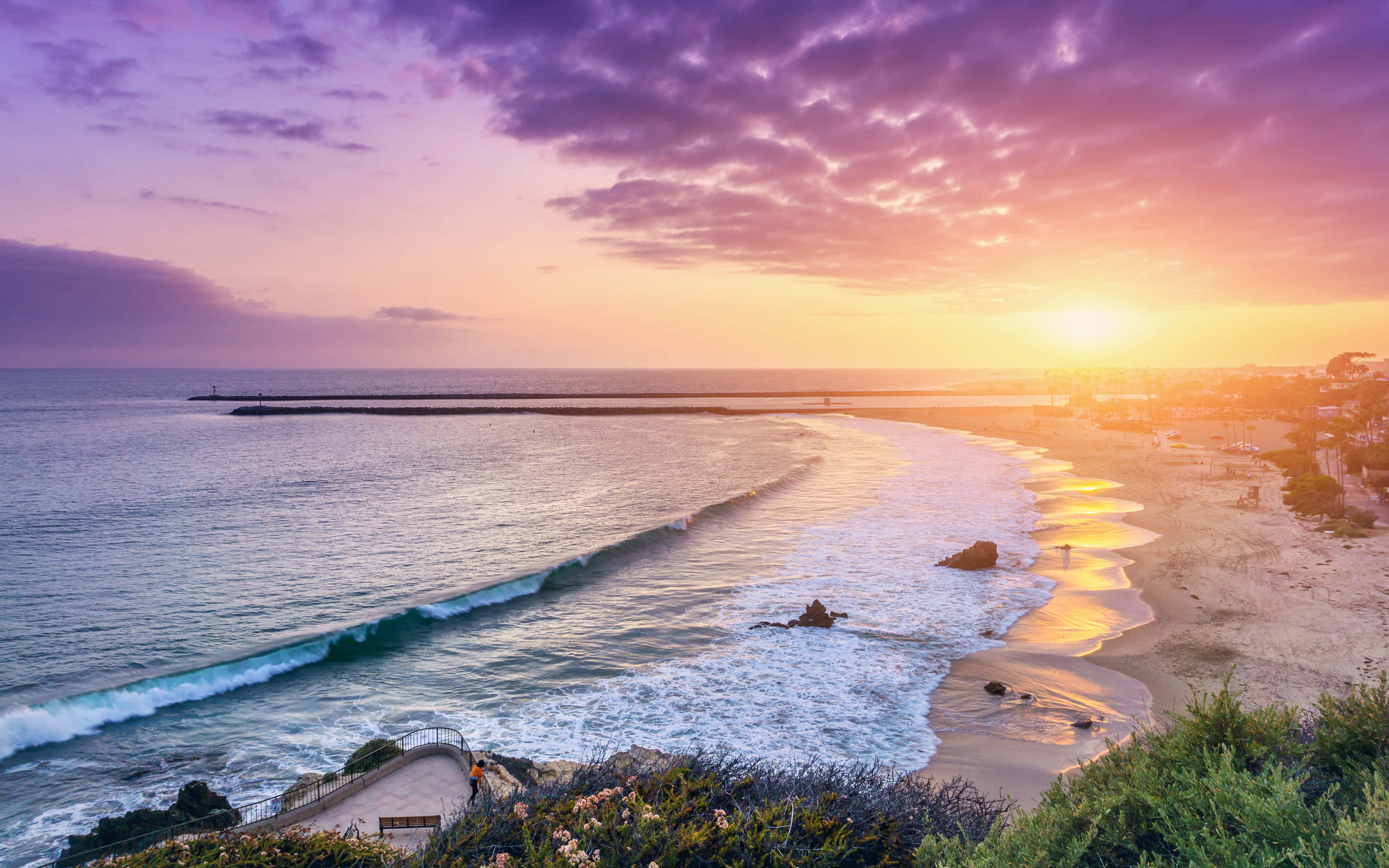 Spanish Beach 桌布 壁紙 — 海岸沙灘上壯麗的日落，海浪拍打金色沙灘，上方有紫橙色雲彩。