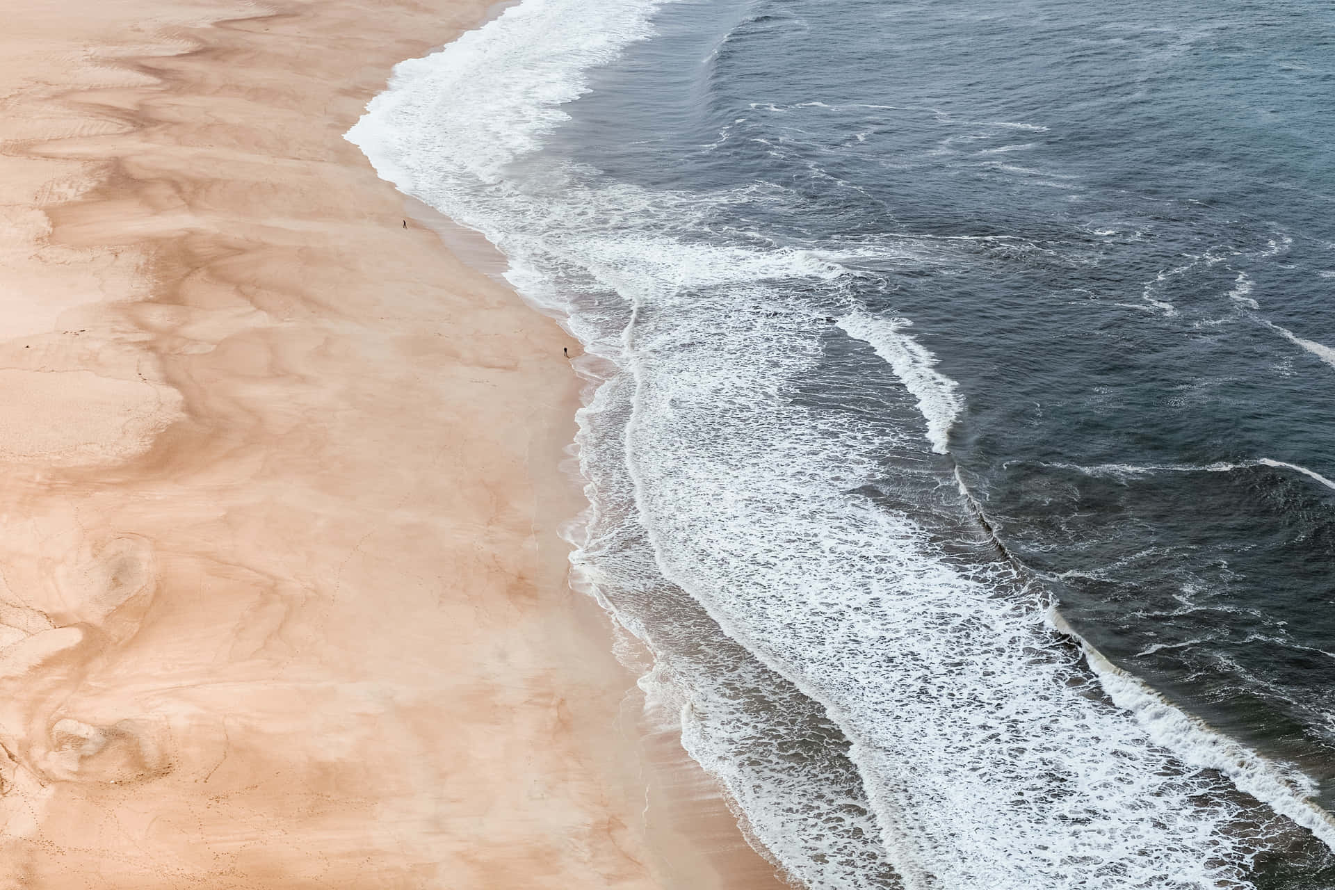 俯瞰海洋波浪與沙灘相遇，濕沙中形成漩渦圖案的航拍視角。