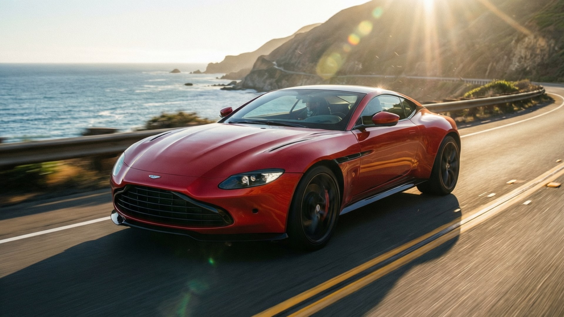 海岸高速V8 壁紙 — 一輛流線型的紅色Aston Martin沿著海岸公路飛馳，背景是海洋懸崖和太陽耀斑。