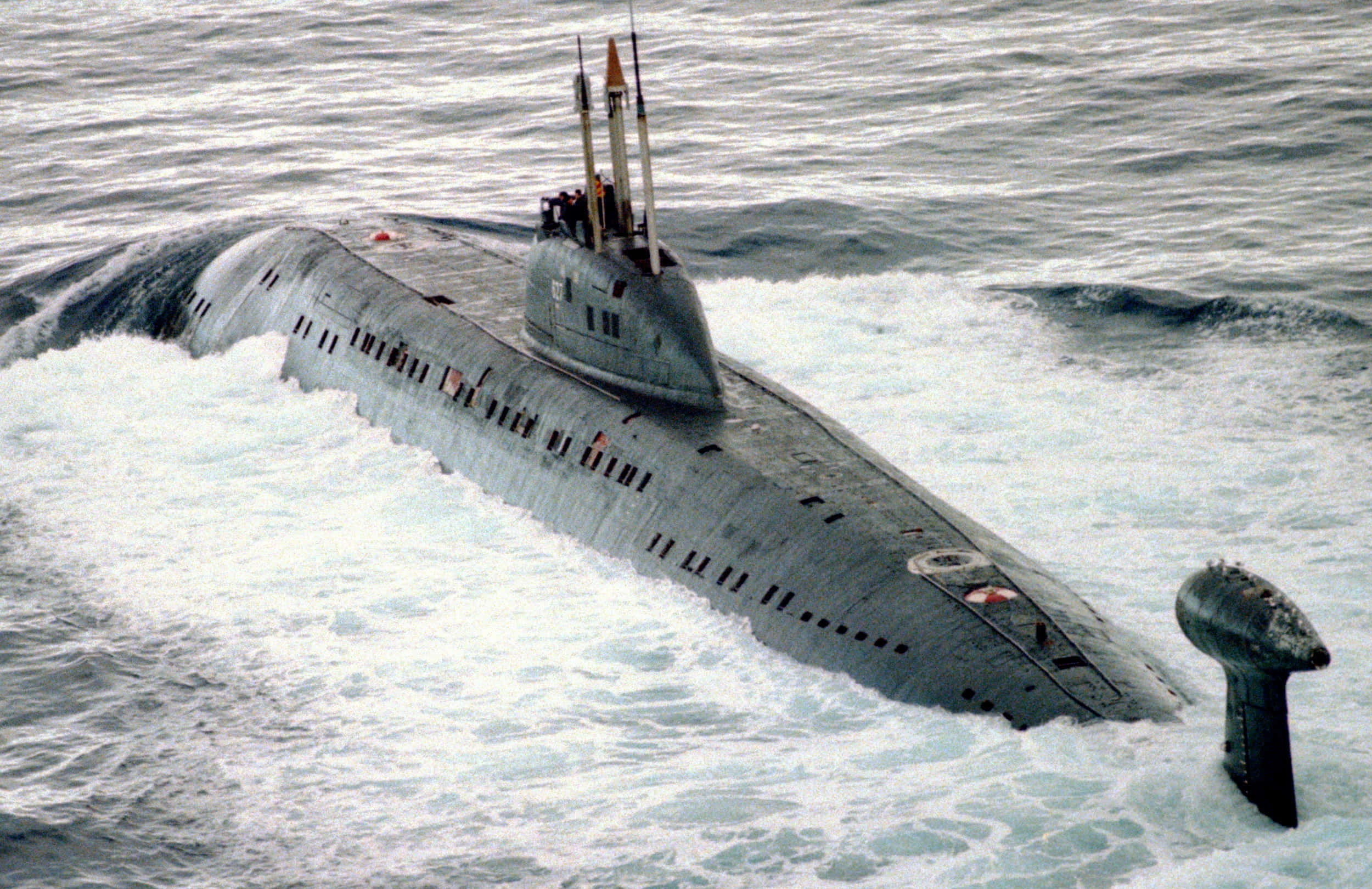 海底冒險即將展開 壁紙 — 一艘灰色軍用潛艇在波濤洶湧的海浪中浮出水面，潛望鏡和導彈發射管清晰可見。
