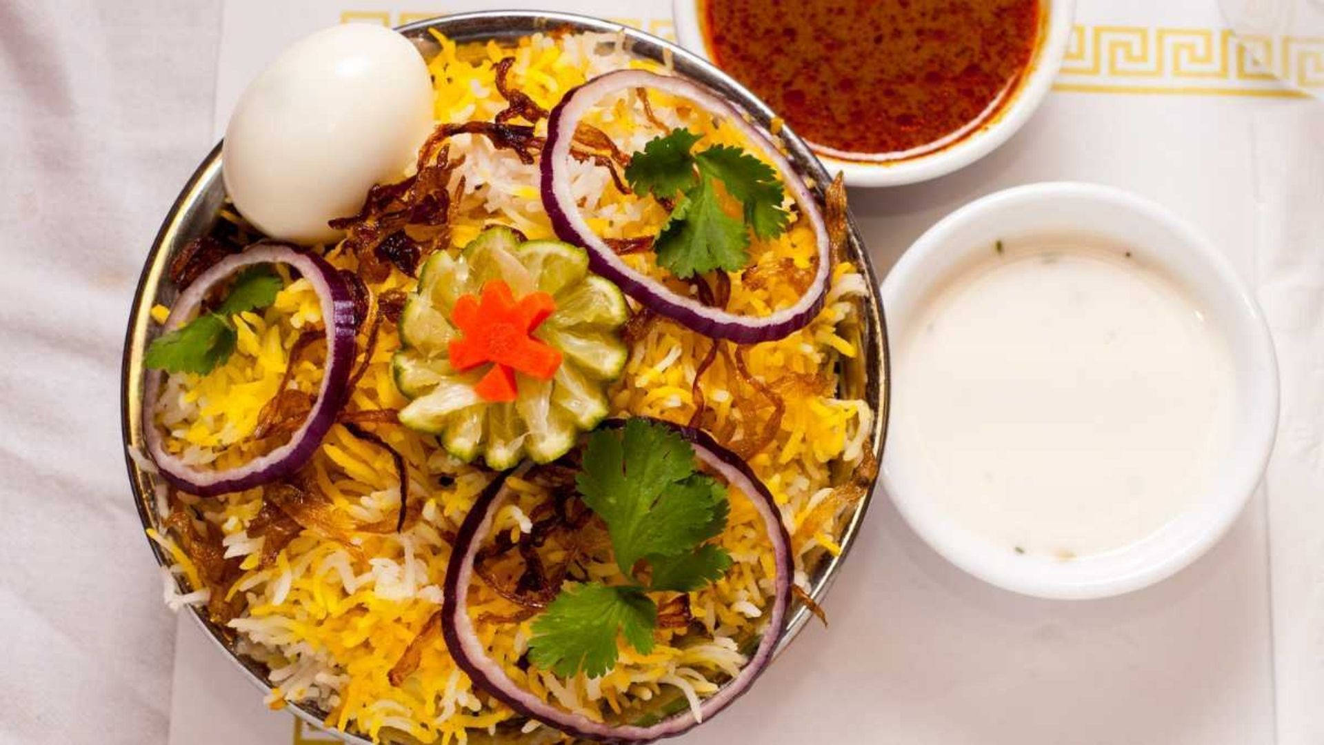 海得拉巴本地美食 壁紙 — 一碗色彩繽紛的印度香飯，上面放有炸洋蔥、青檸、香菜和一個水煮蛋，配以側面醬汁。