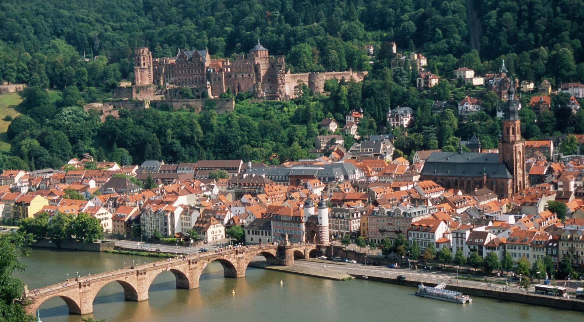 海德堡城堡下的 Neckar 河 壁紙 — 海德堡的鳥瞰圖，其標誌性城堡坐落在鬱鬱蔥蔥的山丘上，俯瞰河流和歷史悠久的城鎮。