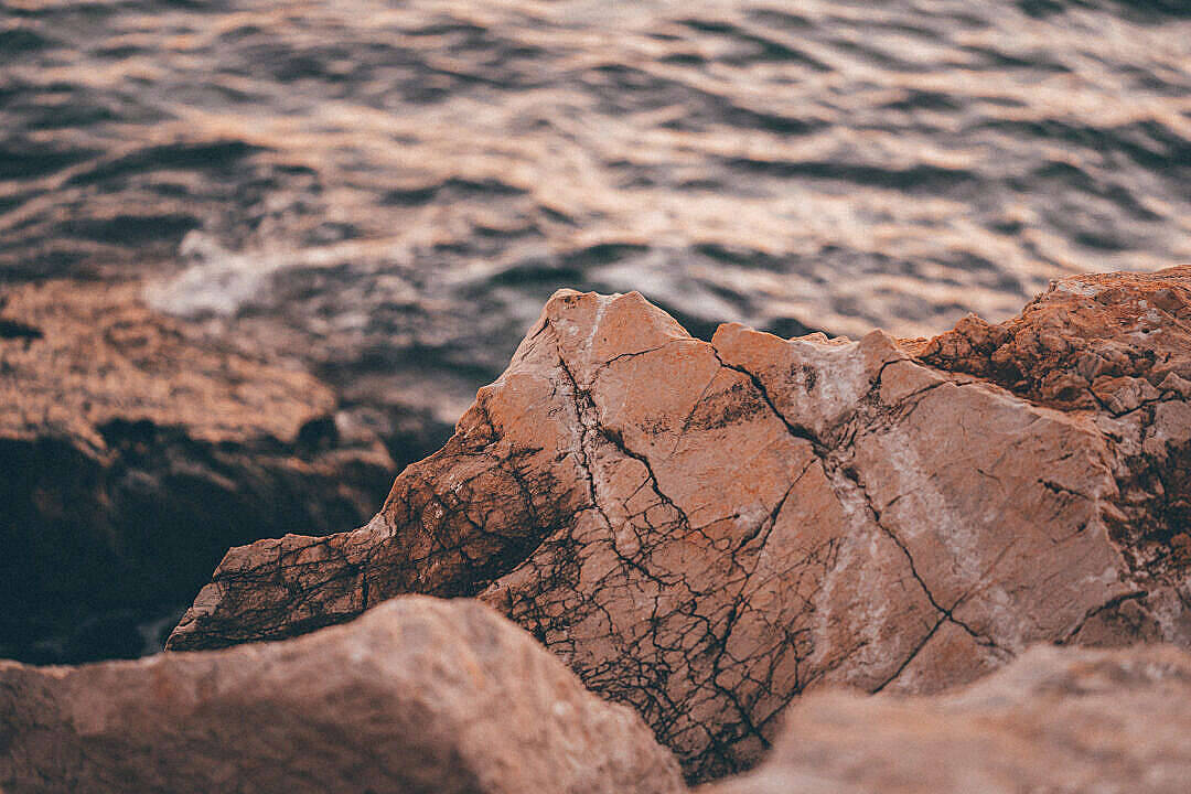 日落時分海邊粗糙的橙色岩石與柔和的海浪。