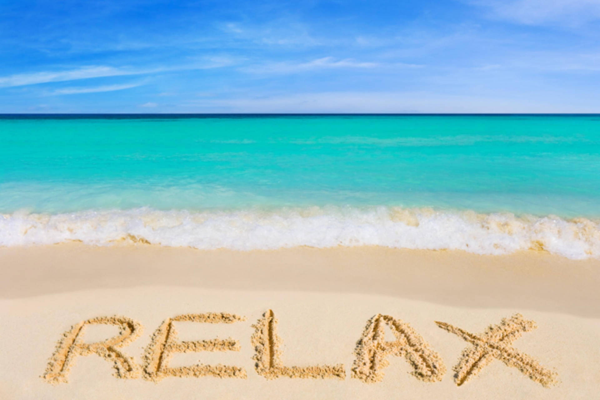 喺熱帶海灘嘅沙上寫住「relax」呢個字，有藍綠色海水同藍天。