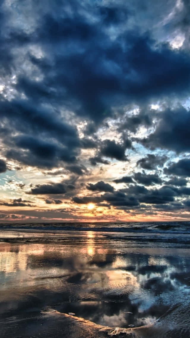 海上日落，雲朵倒映在濕沙上。