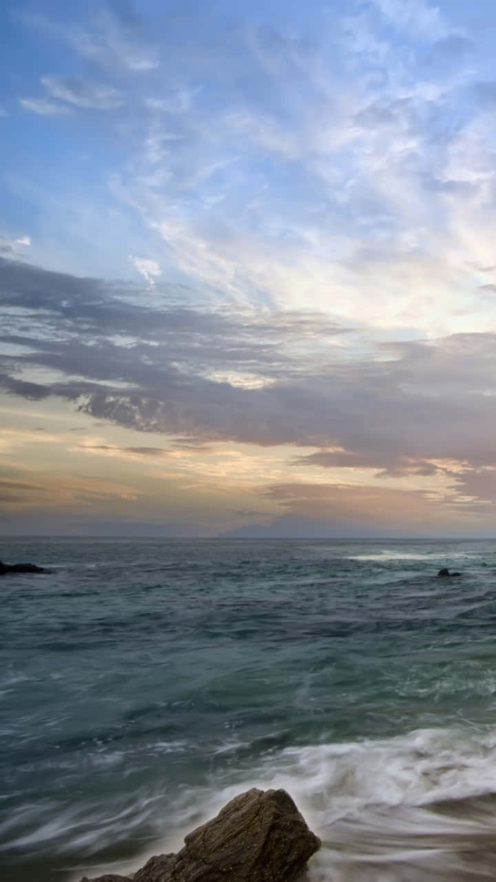 海浪在夕陽下拍打岩石，天空呈現柔和的金色和藍色。