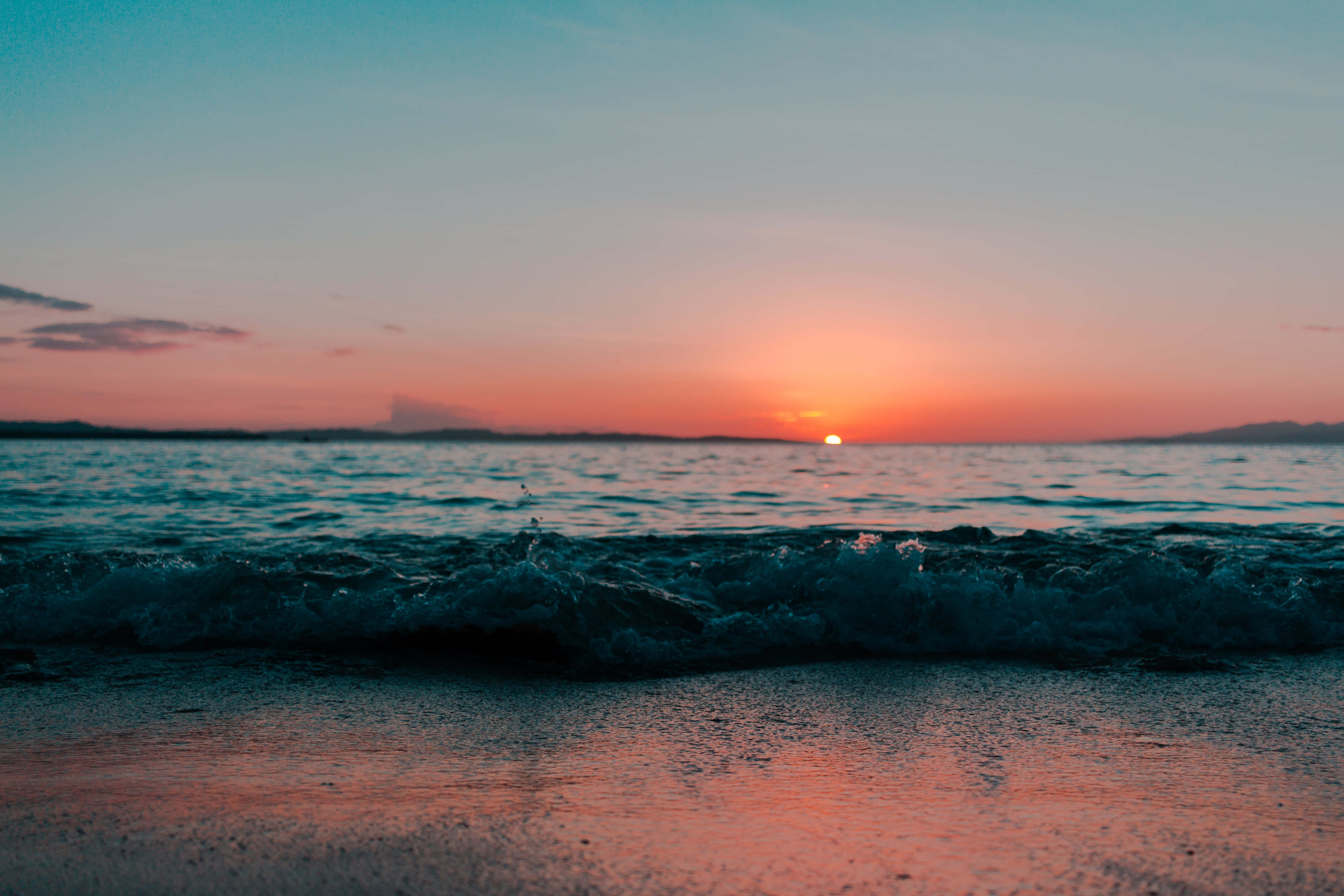 Sunset Ocean 桌布 壁紙 — 海洋上寧靜的日落，海浪拍打沙灘，反射出溫暖的橙色和粉紅色調。