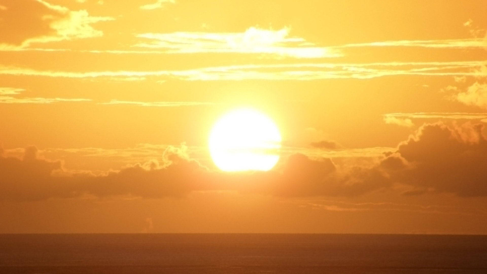 海洋上空的明亮滿月日落 壁紙 — 燦爛的太陽在平靜的海洋上落下，將金色的光芒灑在散落的雲層上。