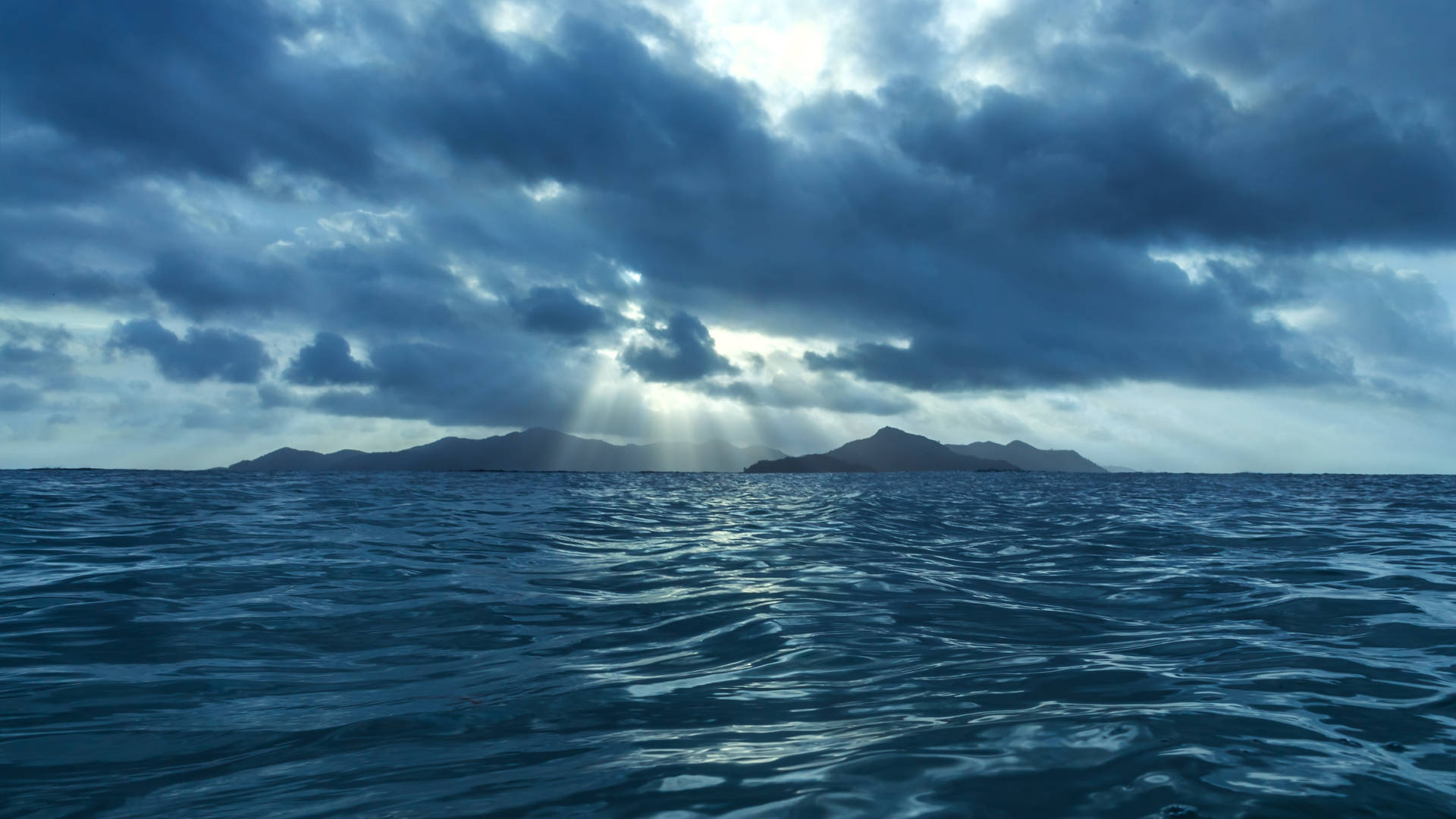 陽光穿過暴風雲，照耀在藍色海洋和遠方的島嶼上。