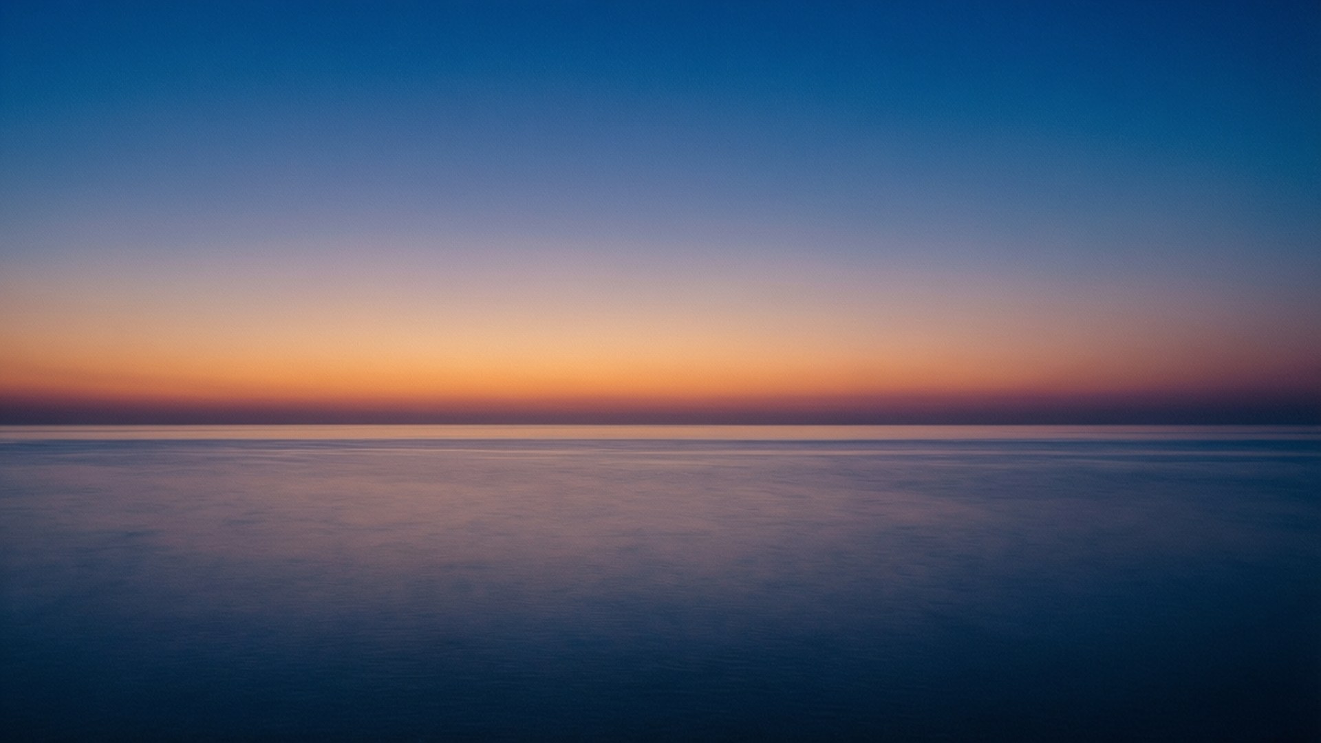 海洋地平線極簡 壁紙 — 寧靜的黃昏地平線，平靜的海洋與深藍色和柔和橙色的漸變天空相遇。