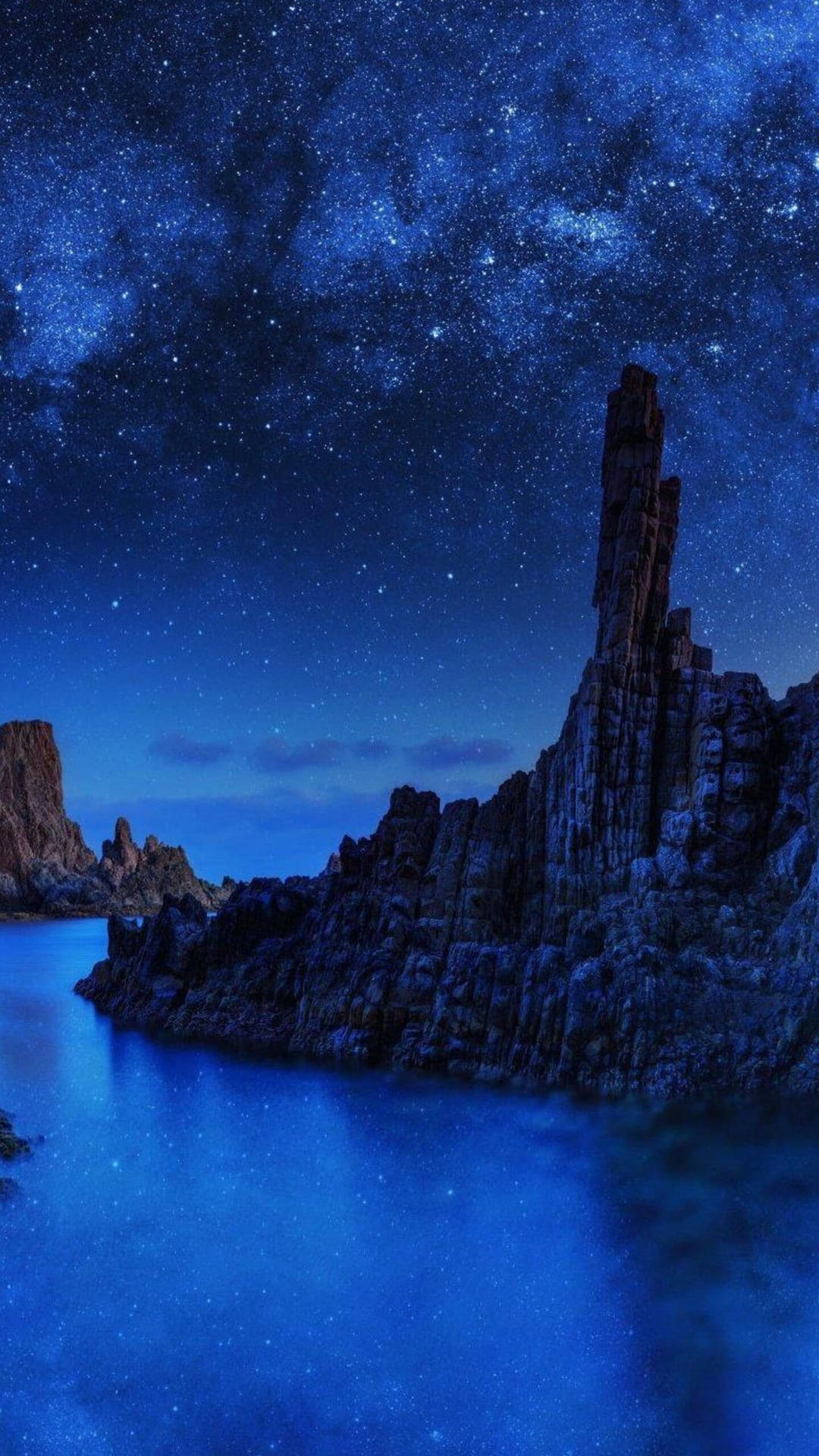 繁星點點的夜空，岩石懸崖和平靜的水面反射星星