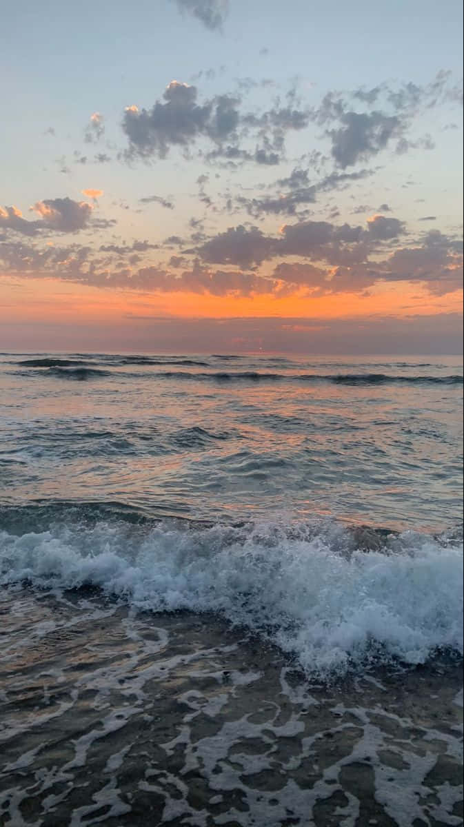在色彩繽紛的夕陽下，海浪拍打著海岸，天空有散落的雲朵。