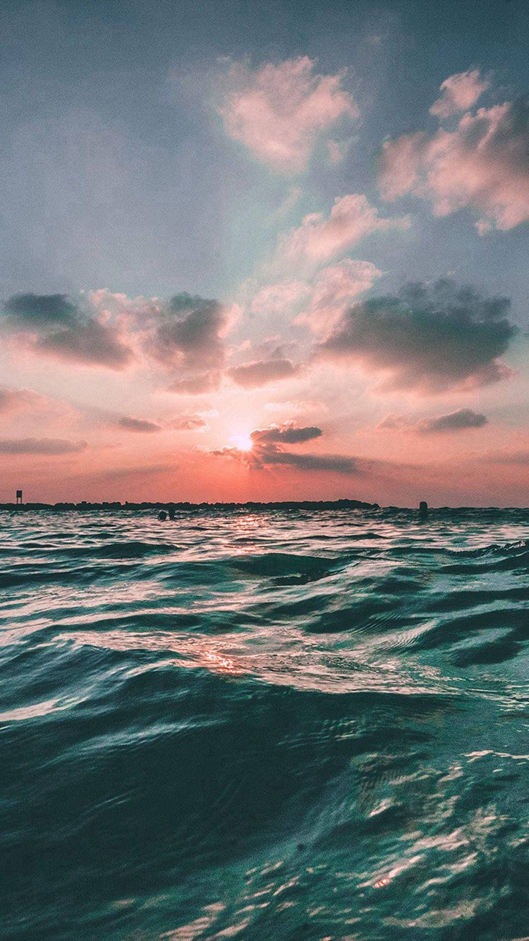 海洋日落 iPhone 6s Plus 壁紙 — 夕陽將天空染成粉紅色和橙色，並反射在漣漪的藍綠色海浪上。
