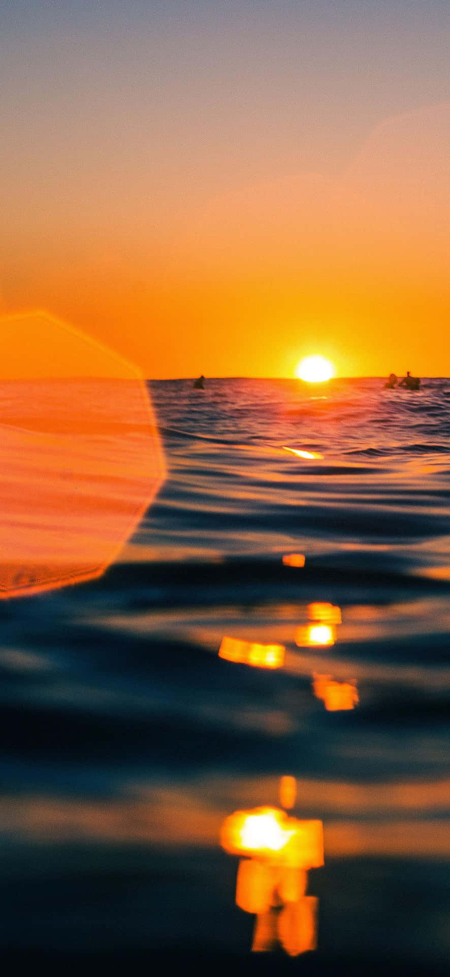 夕陽下的海洋，有衝浪者和鏡頭光暈