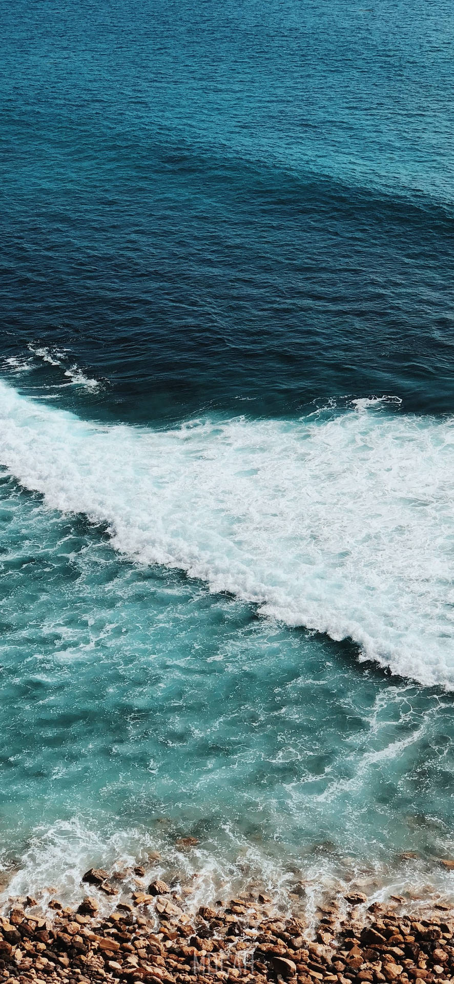 綠松石色的海浪在晴朗的天空下拍打岩石海岸線。