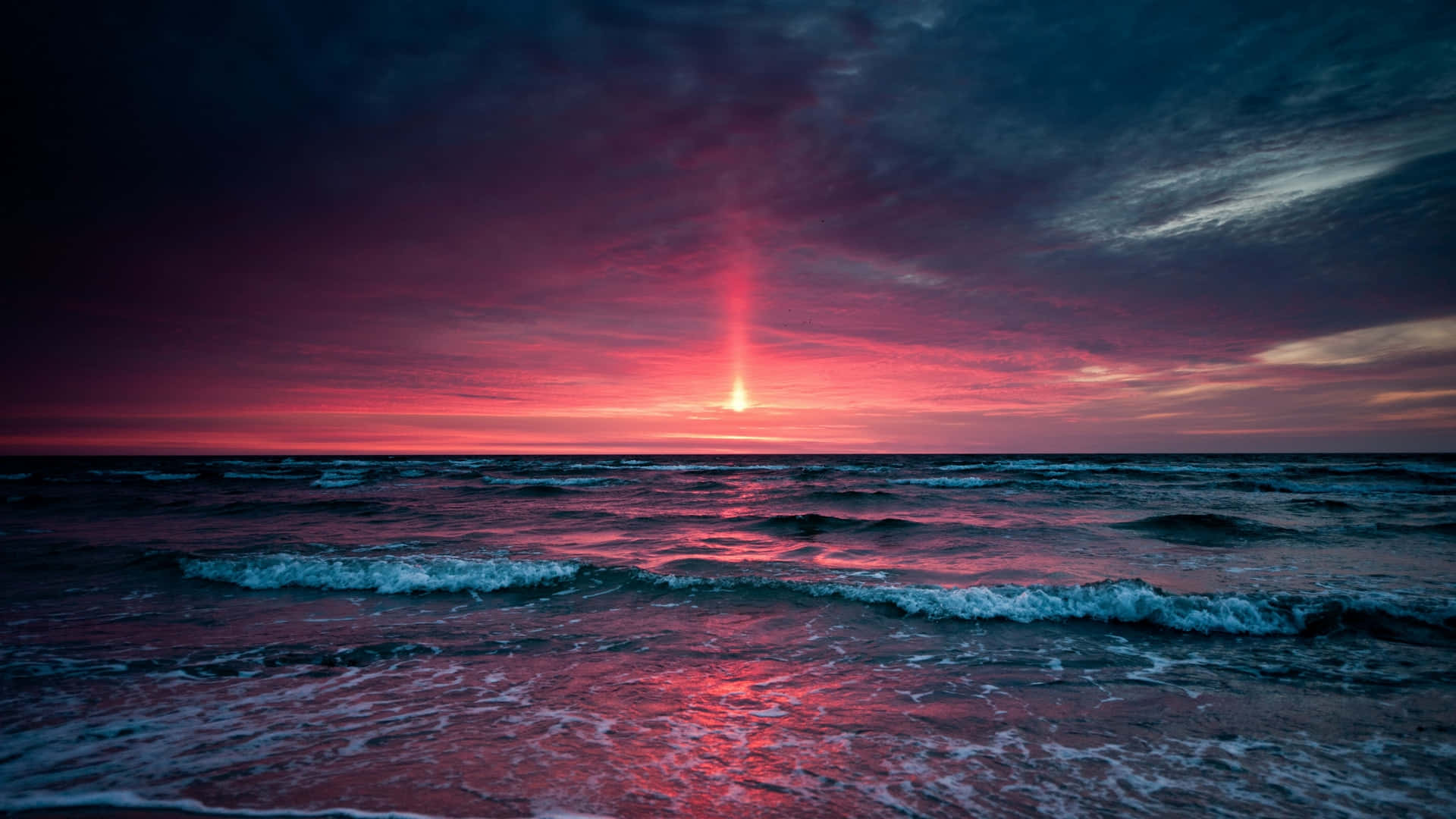海洋灘日落的迷人景色 壁紙 — 海面上戲劇性的日落，火紅和深紫色的雲彩映照在洶湧的海浪上。