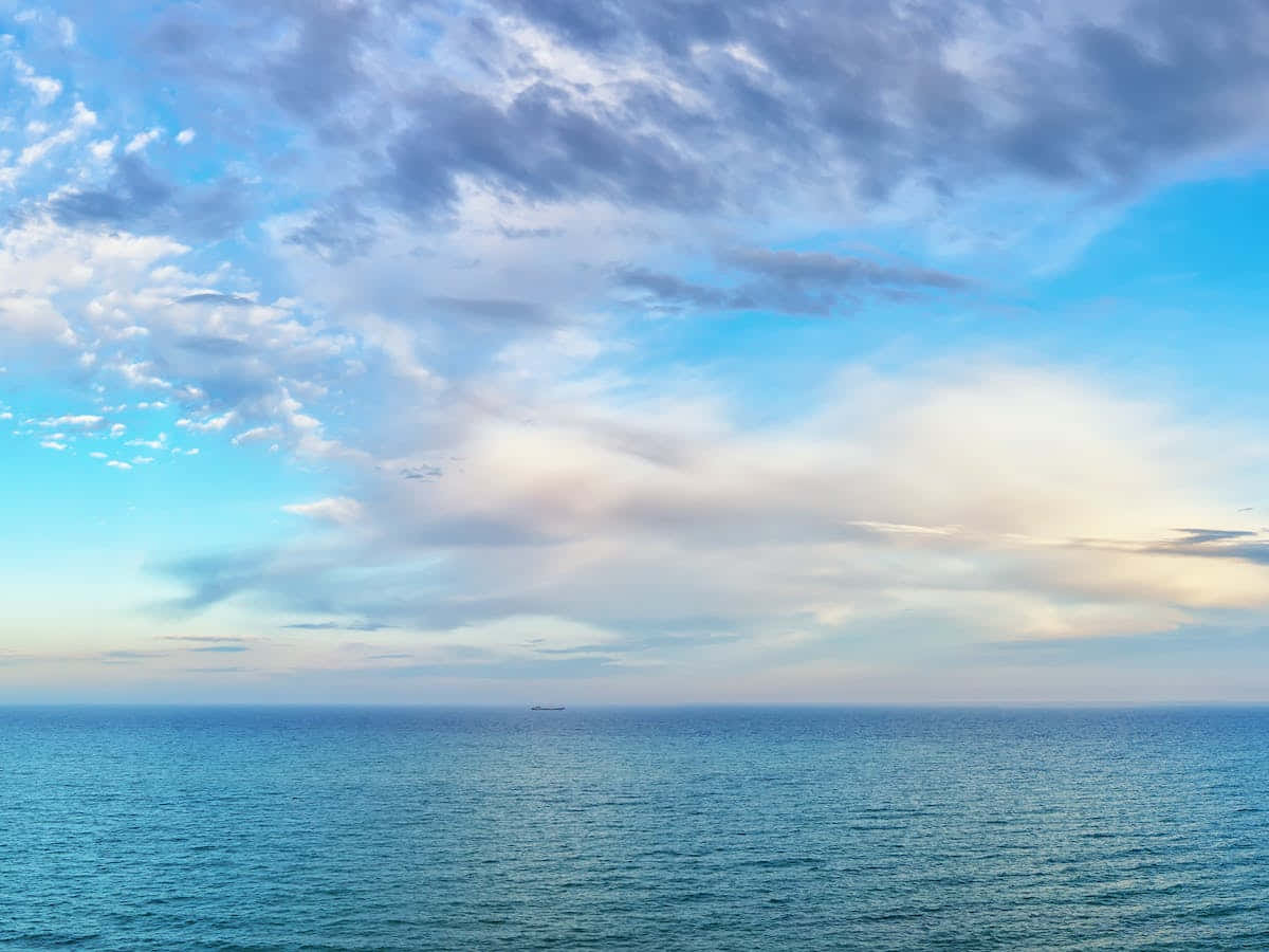 海洋的碧綠色水色依然莊嚴而神秘 壁紙 — 廣闊海洋與天空相接，散落的雲朵和遠處的船隻在平靜的碧綠海面上。