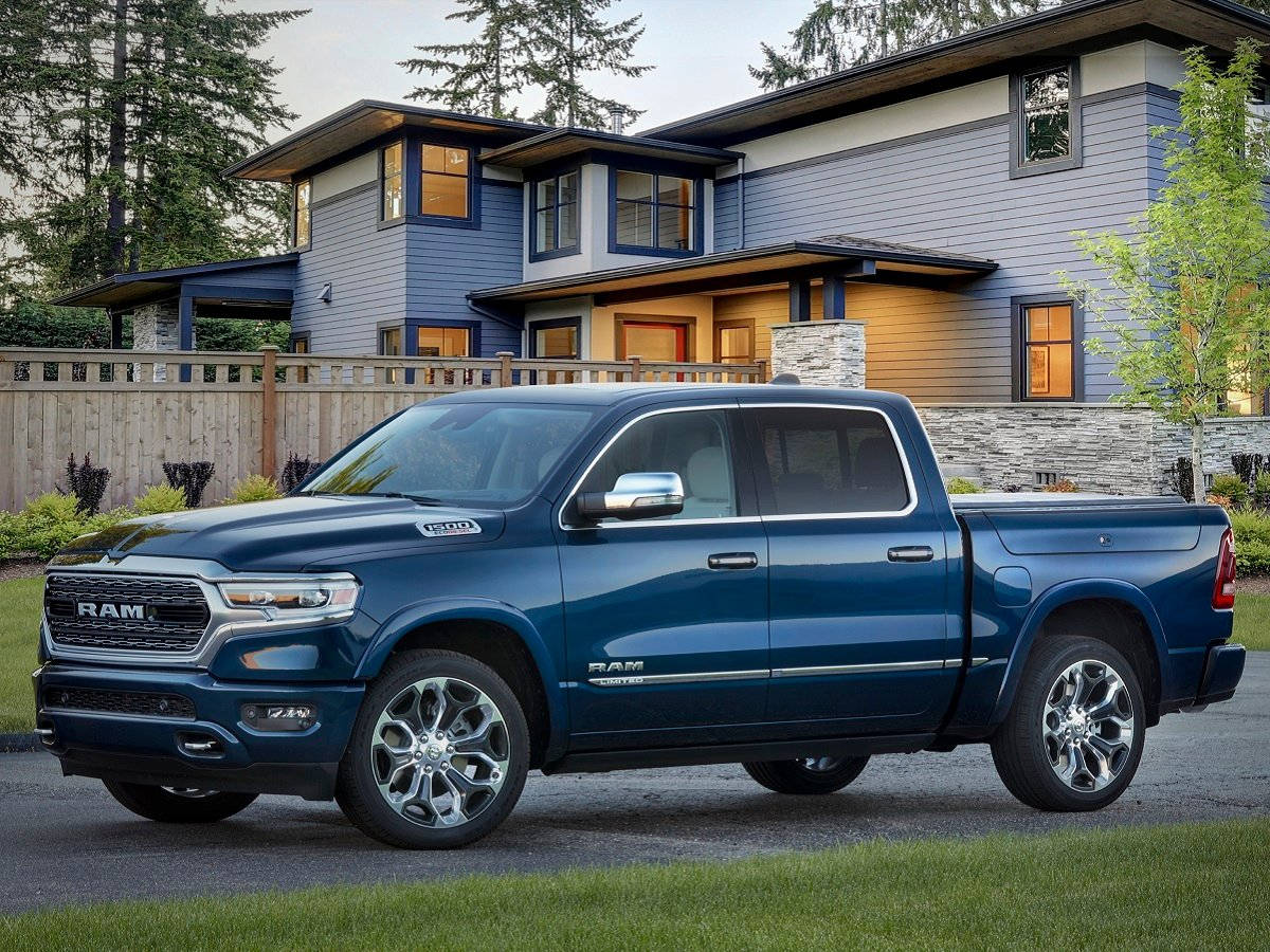 海洋藍 RAM 1500 卡車 壁紙 — 一架時尚的藍色Ram皮卡車停在一棟現代藍色房屋前，房屋有溫暖照亮的窗戶和周圍的樹木。