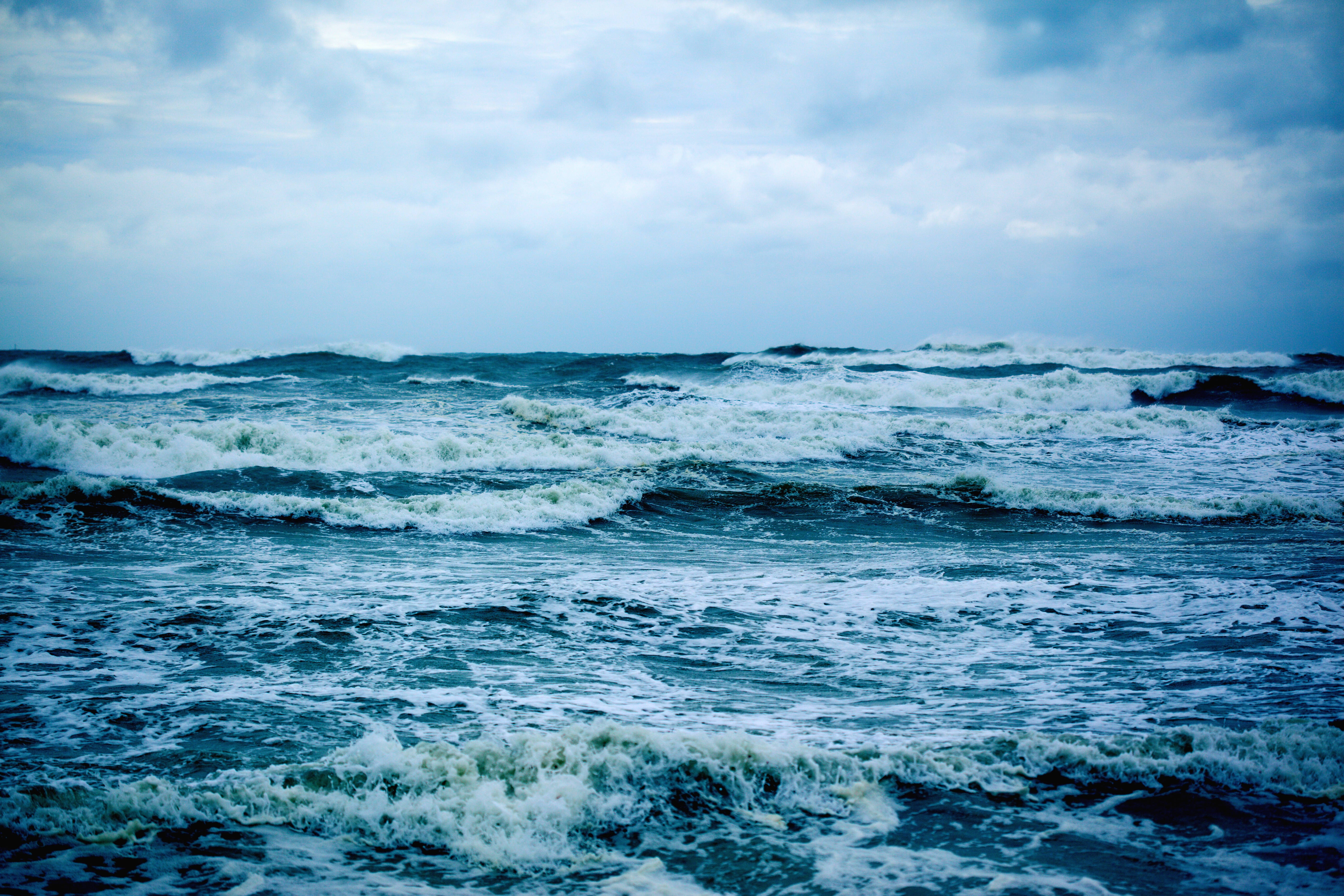 海浪暴風 壁紙 — 翻騰的海浪在陰雲密佈的天空下撞擊，形成戲劇性的藍色調海景。