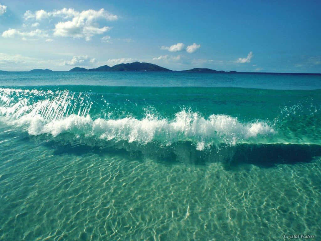 清澈的藍綠色海洋波浪帶著白色泡沫衝擊，露出沙質底部，上方是晴朗的天空。